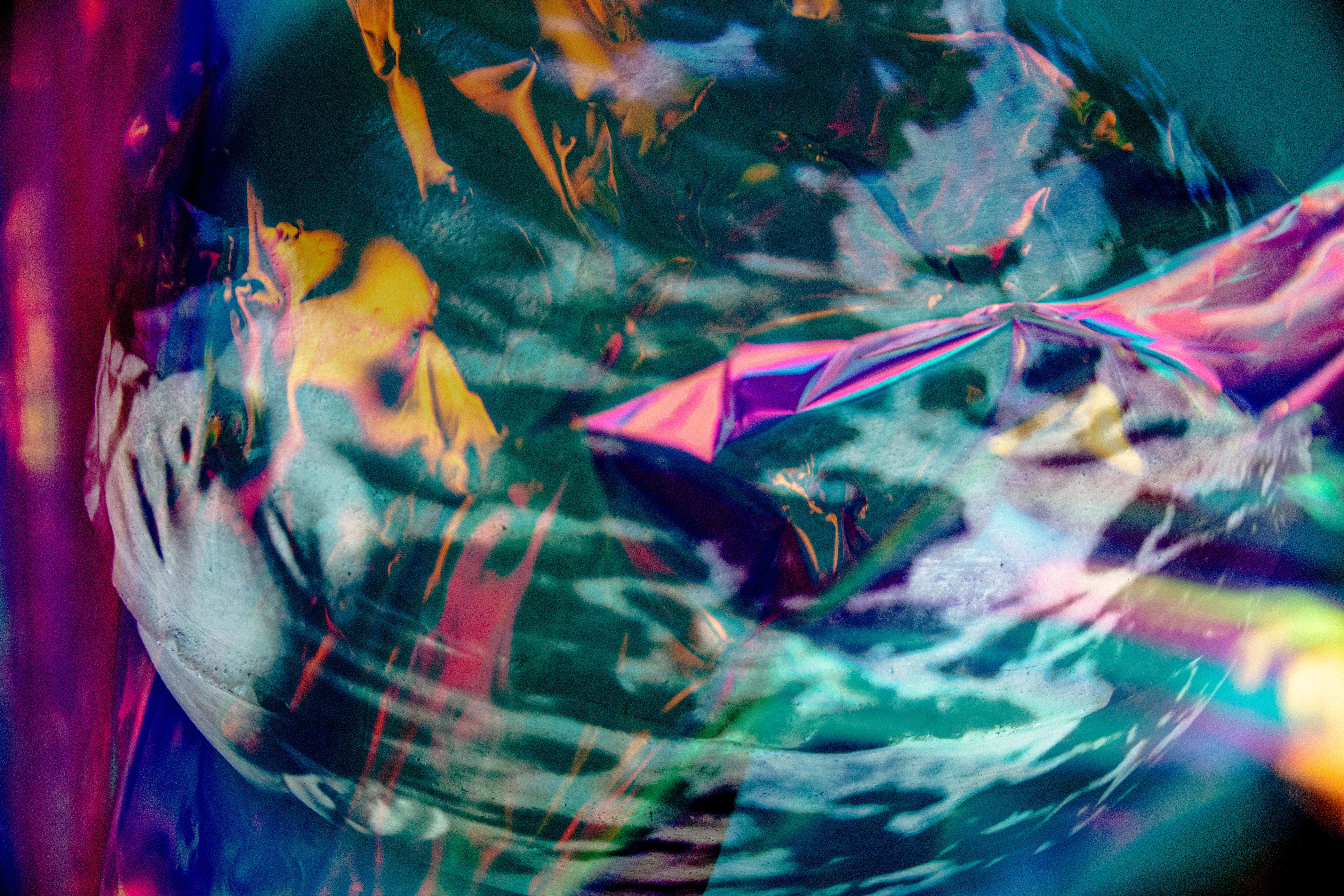 A pale face with a hand pressed against it at the left, under teal and navy foil with orange and pink patches.