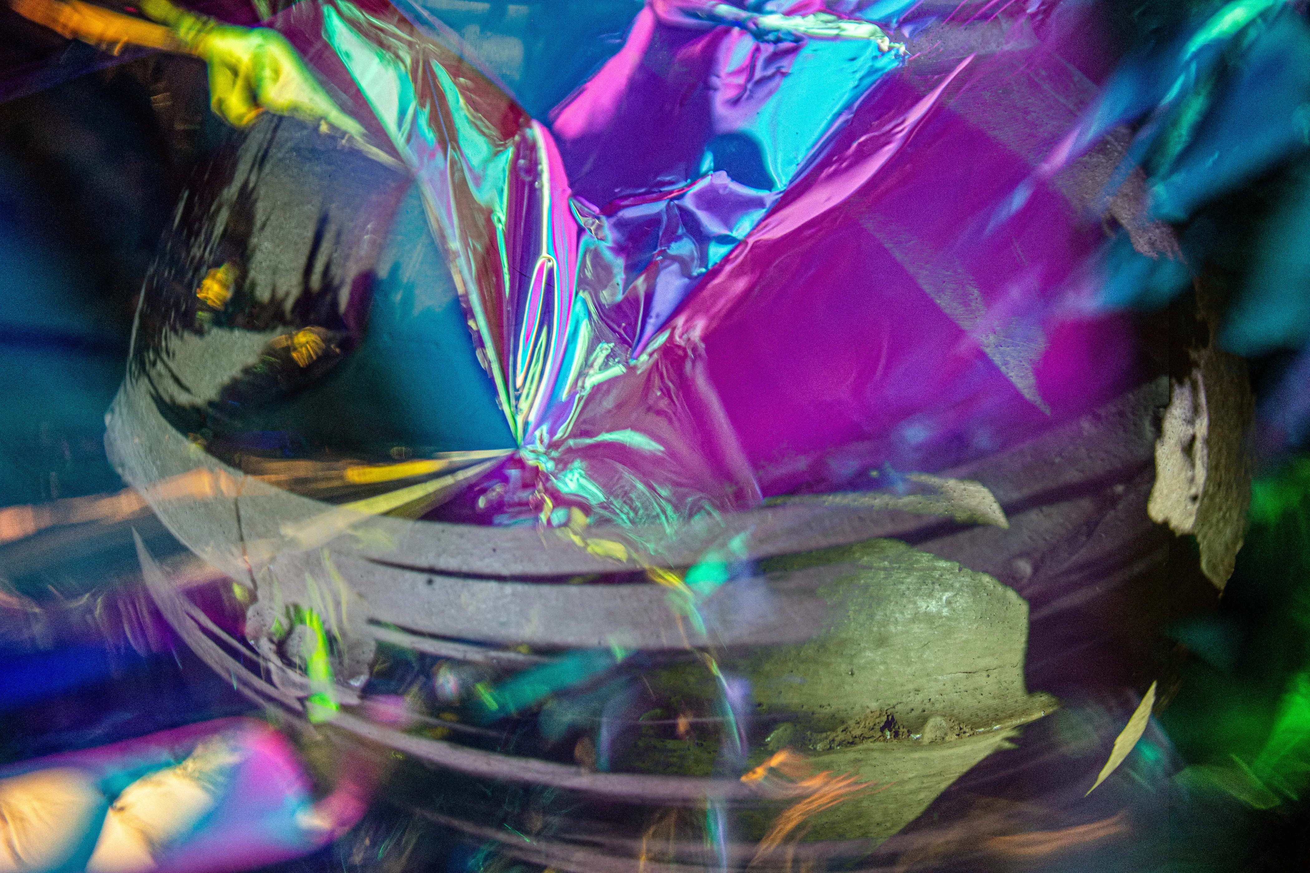 Purple, green and teal foil with pale curved bands across the lower half and a pale face fragment at the right edge.