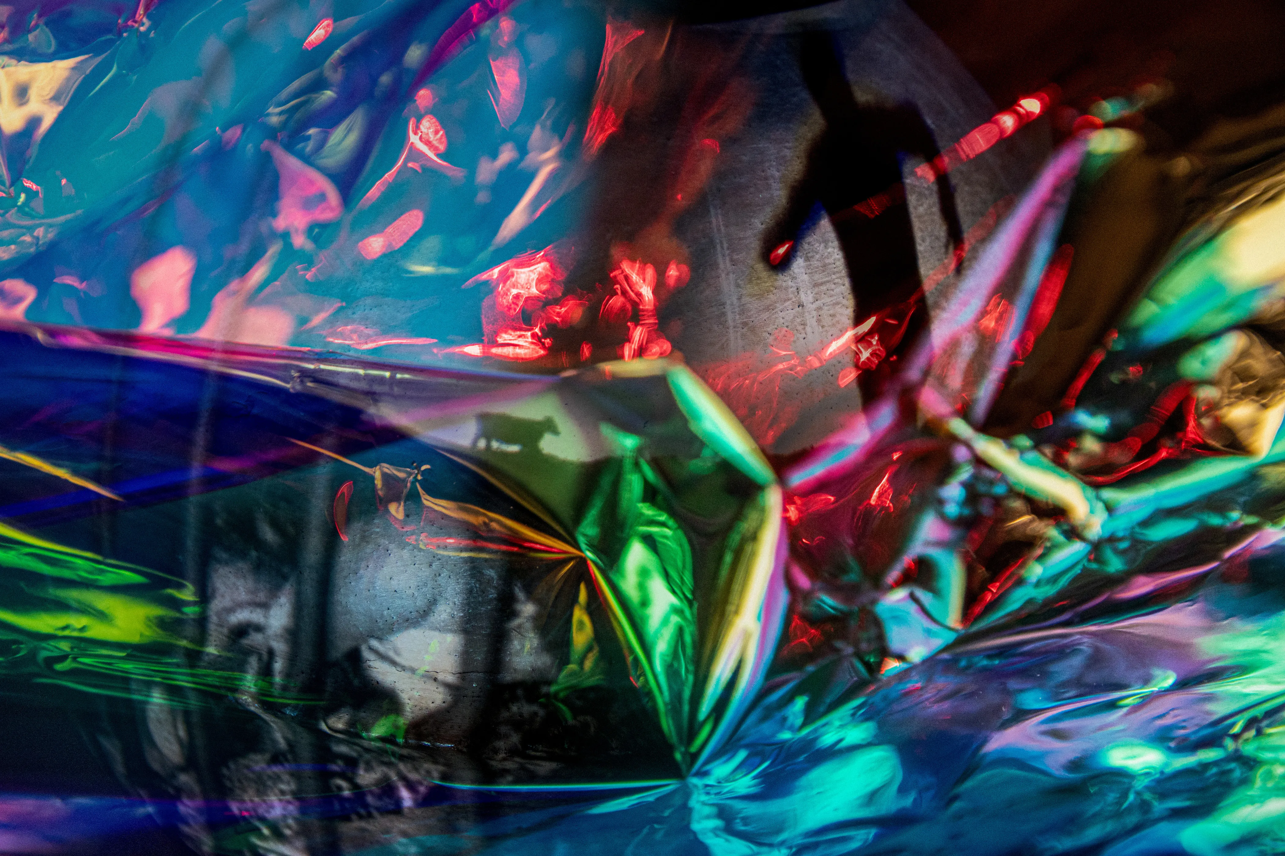 A dark standing figure at the upper right above green, pink and blue foil, with a pale face at the lower left.