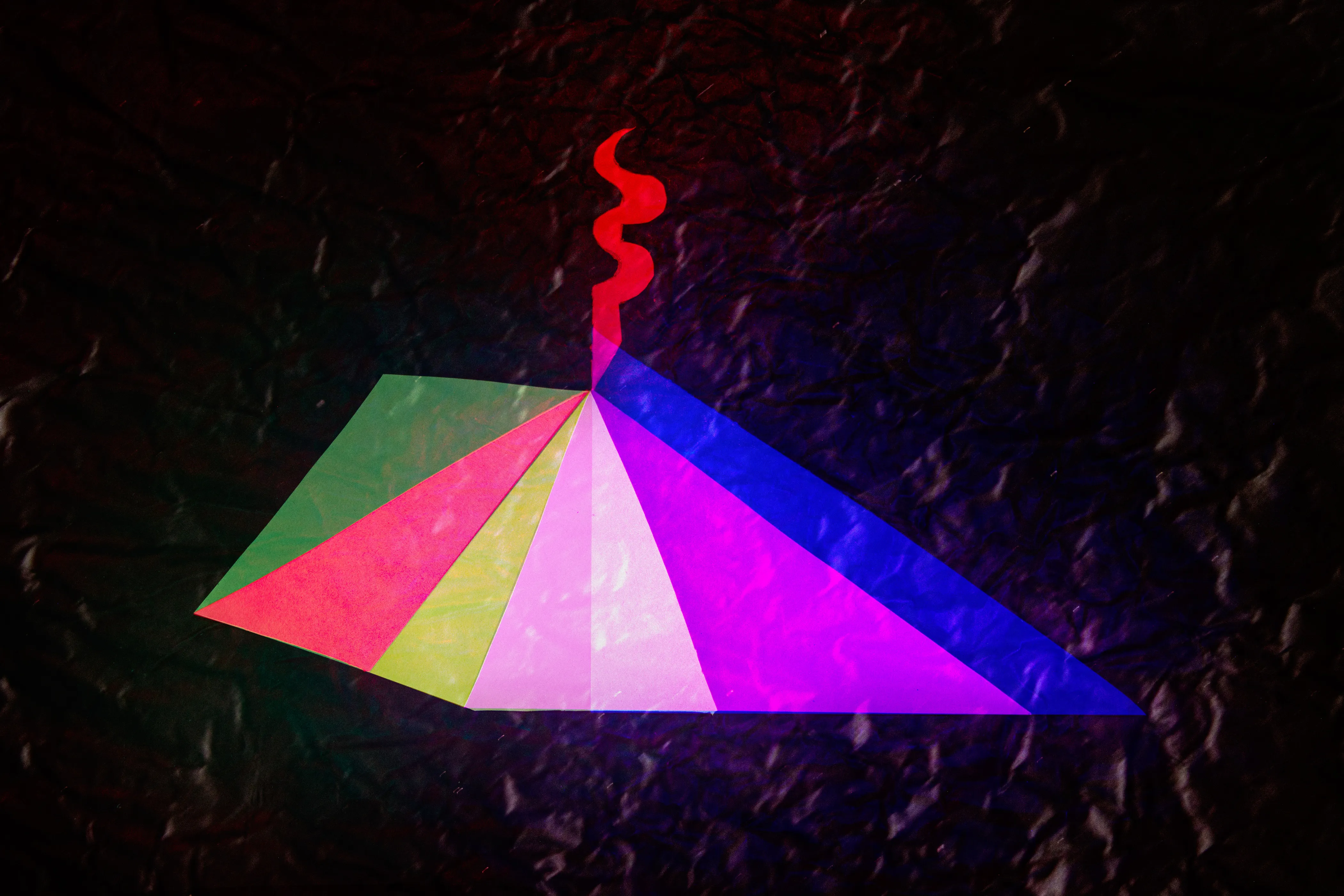 A wide triangle of overlapping pink, yellow, green and blue translucent panels, with a thin red squiggle rising from its peak.