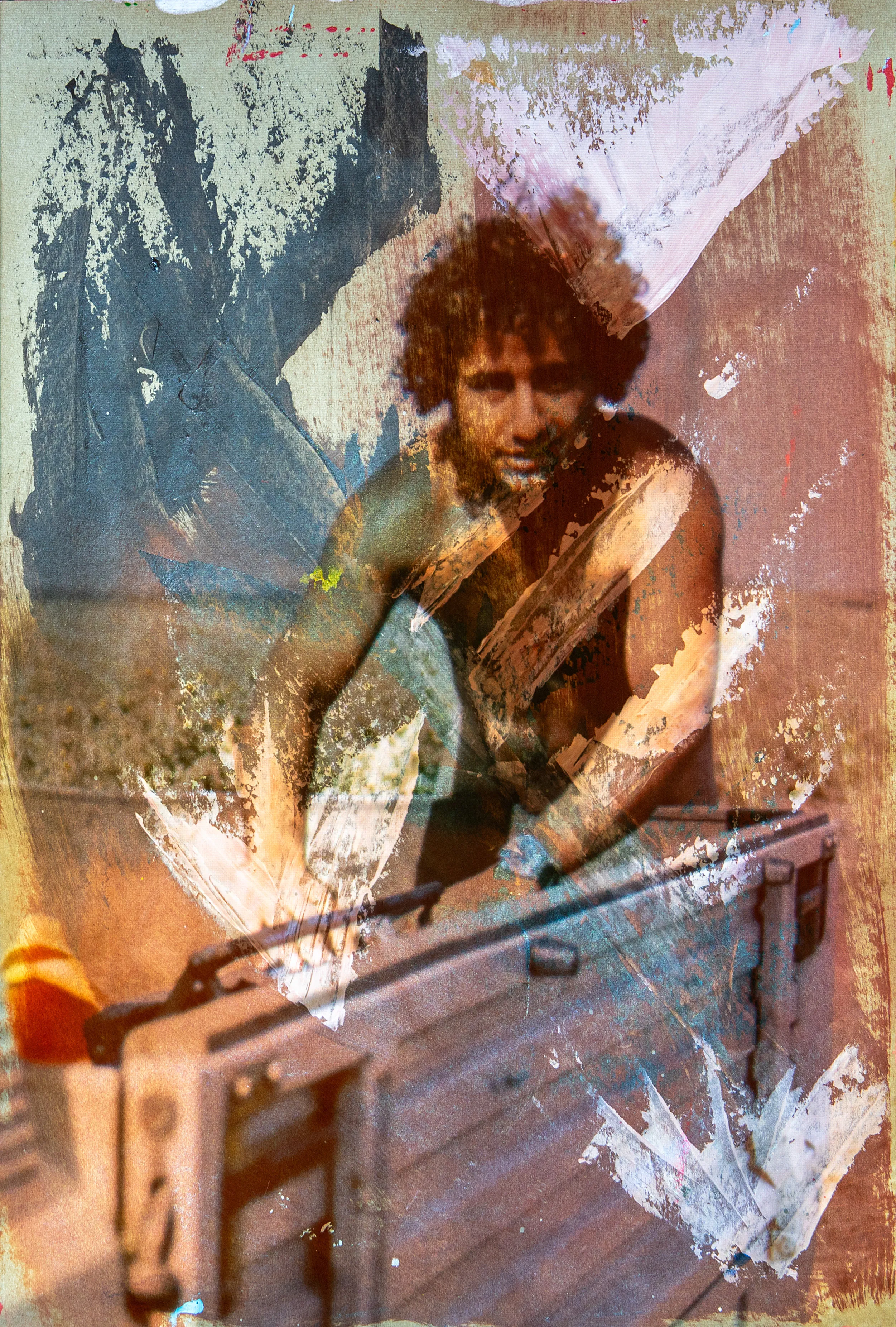 A man with curly hair leans over a large case, framed by white and gray paint marks.