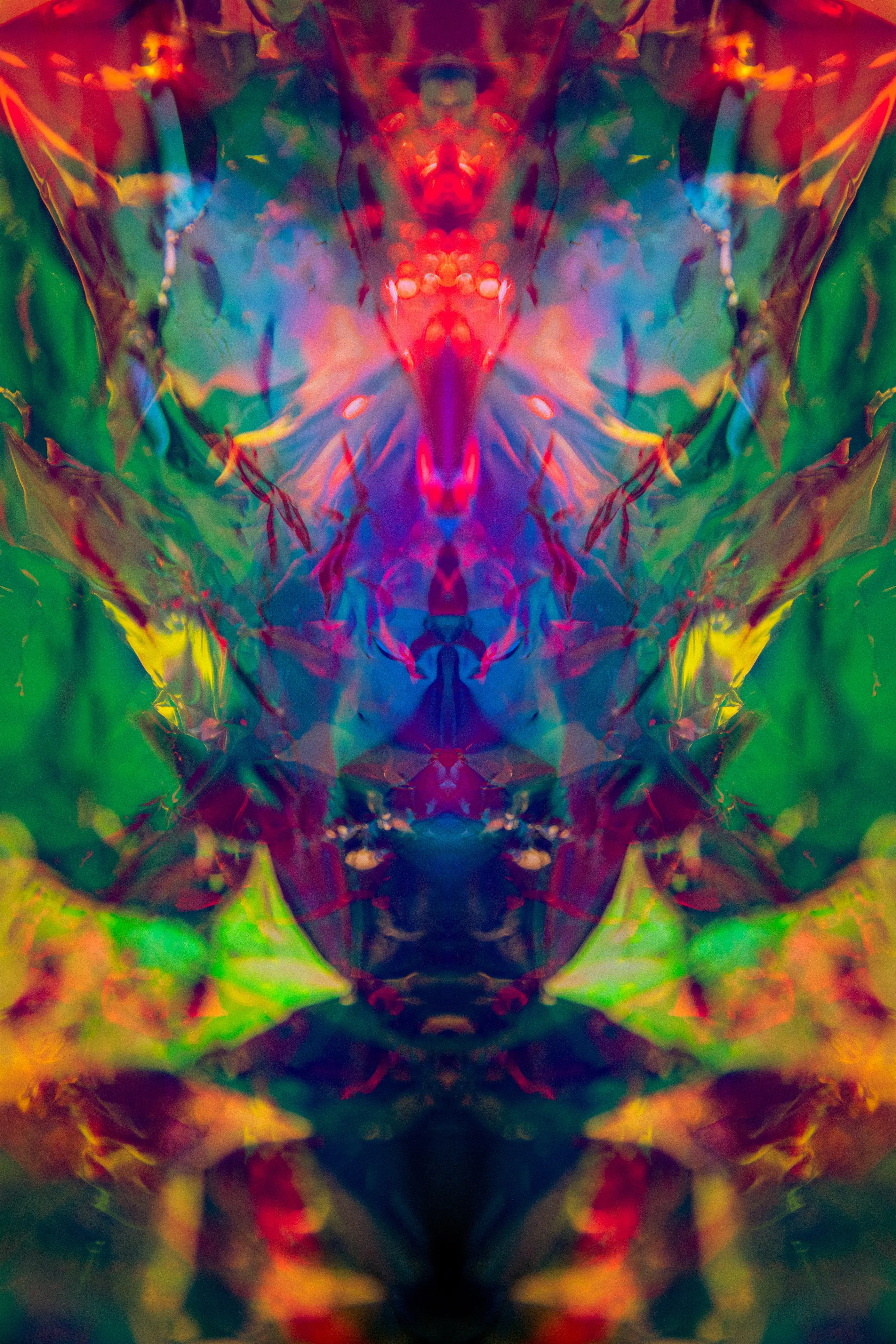 A tall mirrored composition in red, green, blue and yellow, symmetrical around a central axis, with a darker shape low in the middle.