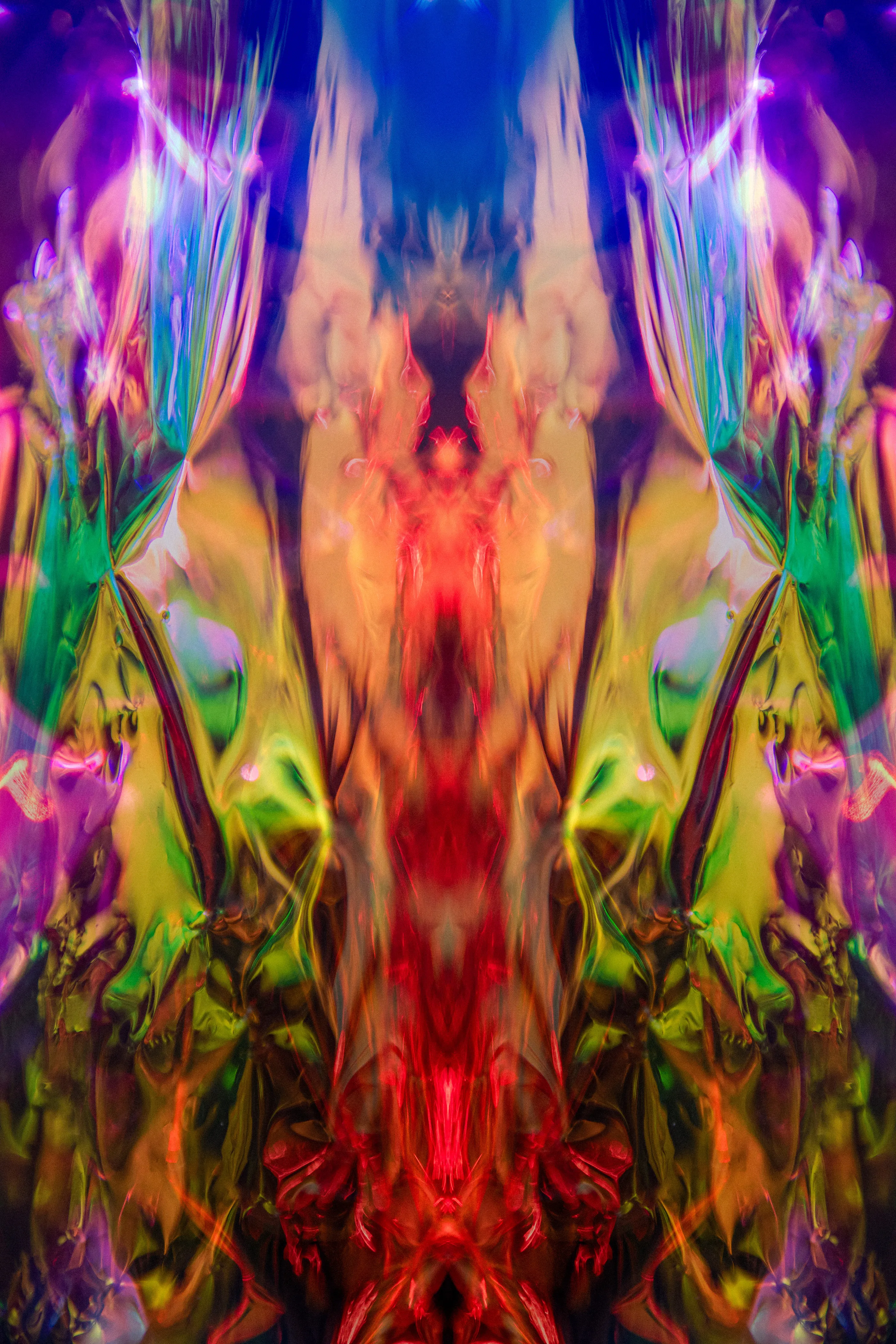 A tall mirrored composition in orange, yellow, purple, green and red, symmetrical around a warm central column.