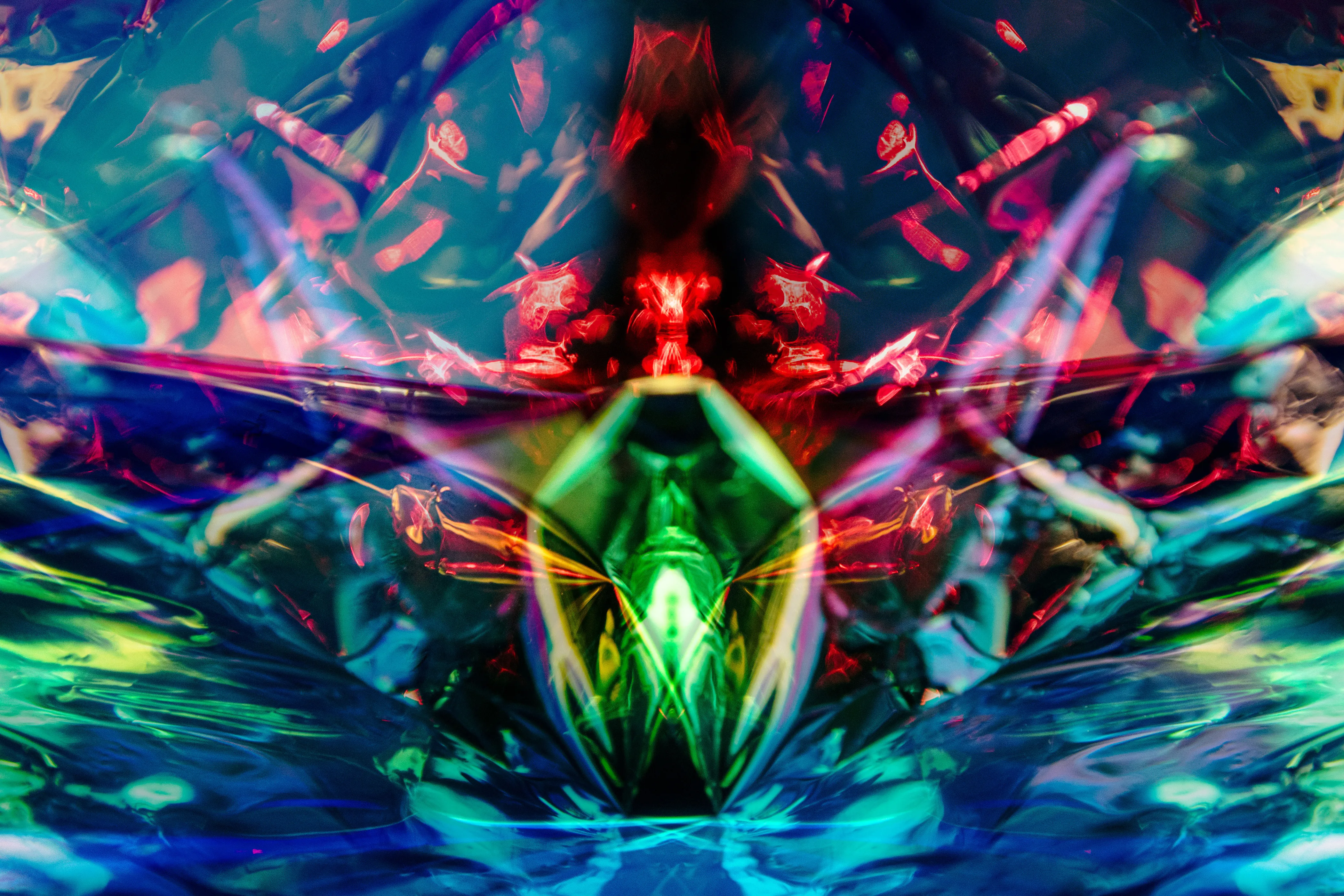 A wide mirrored composition in teal, blue and green with red at the center and a green faceted shape below it.