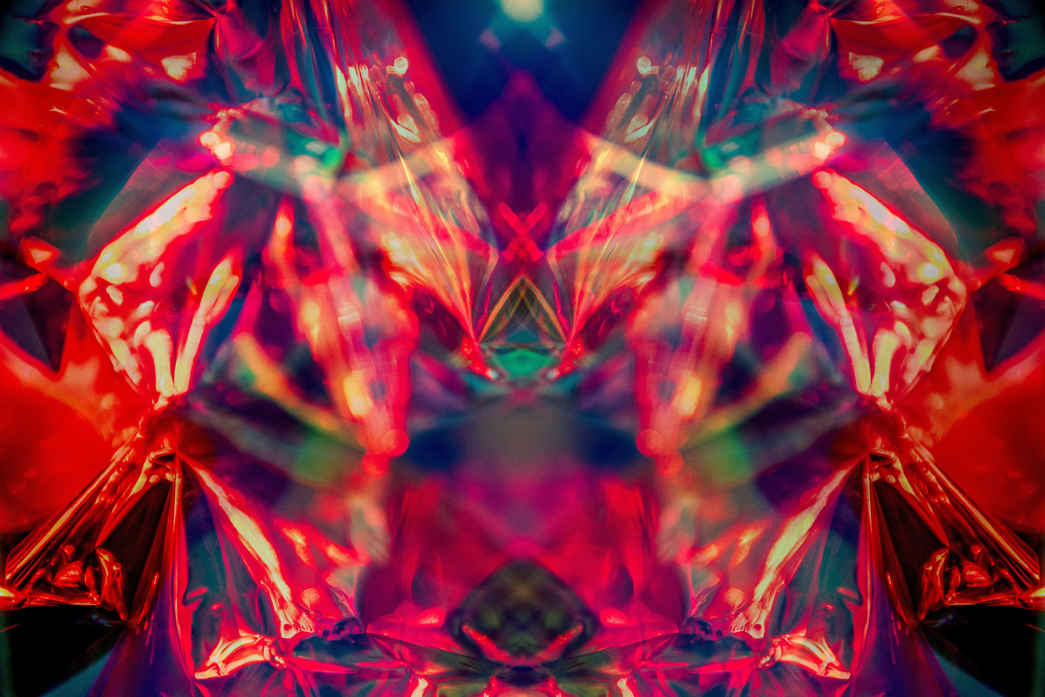 A wide mirrored composition in red, orange and pink with pale highlights, symmetrical around a dark central gap.