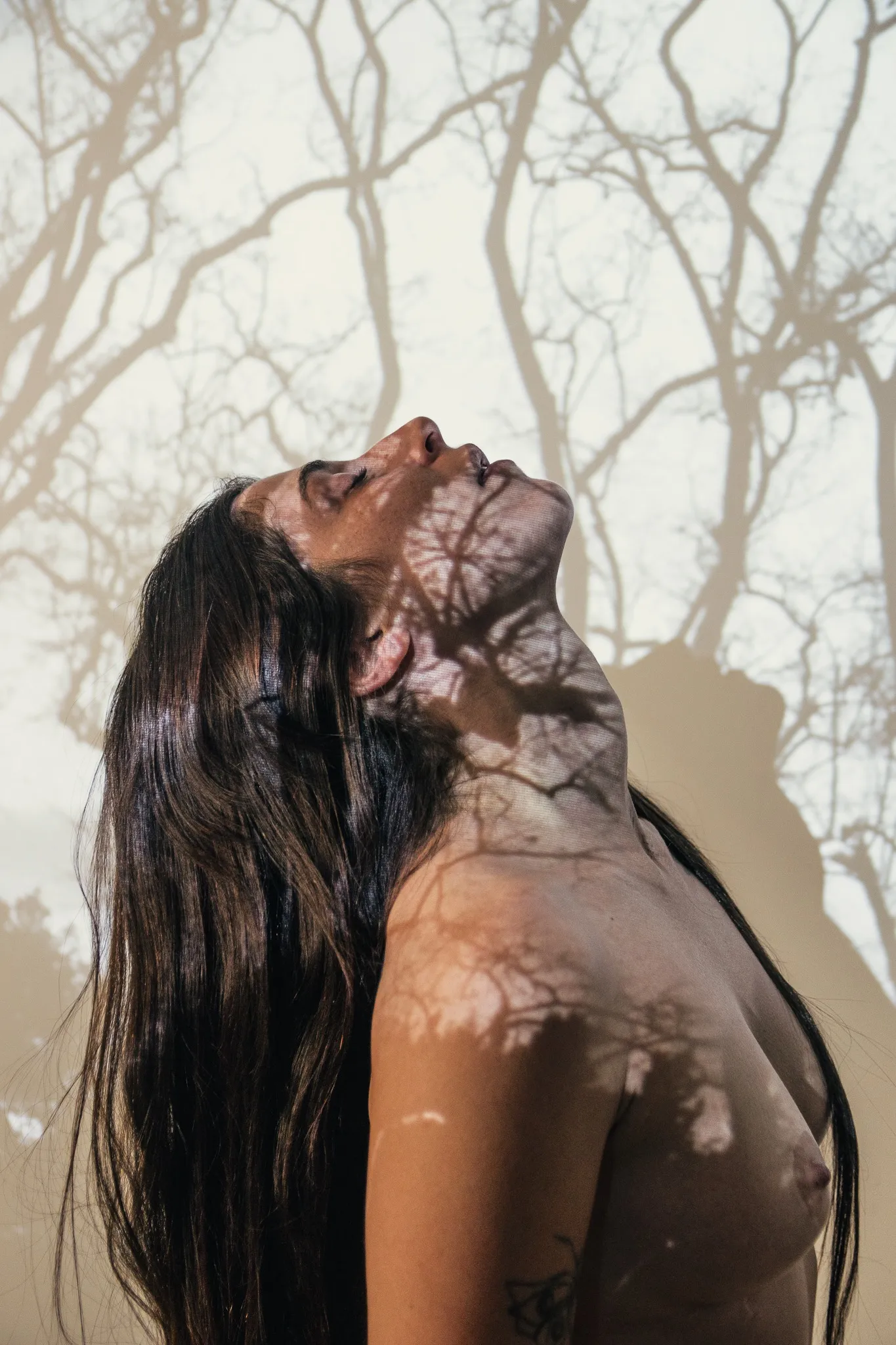 A close view of a figure with the head tilted back and eyes closed, branch shadows across the face and shoulder.
